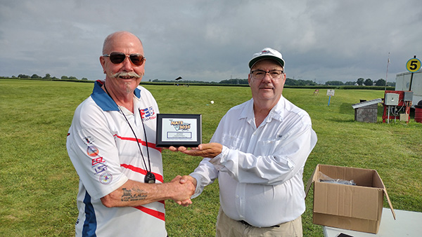 Two men shaking hands, one holding an award plaque, outdoors.