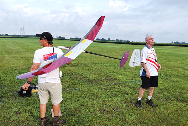 Two men standing on a grassy field with a model glider.