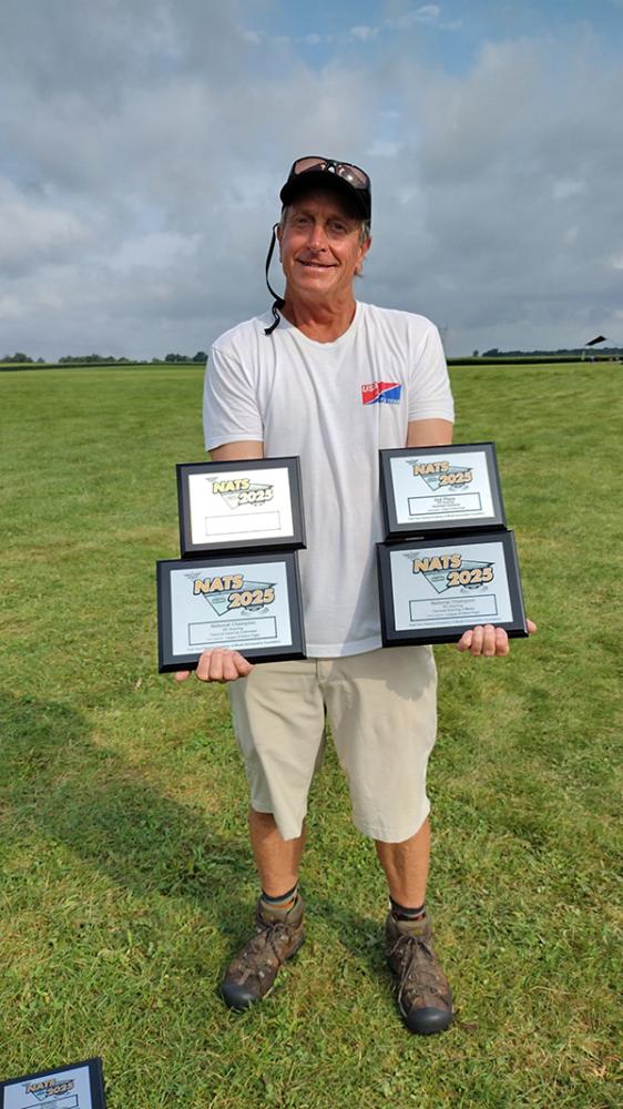 Man holding multiple award plaques on a grassy field.