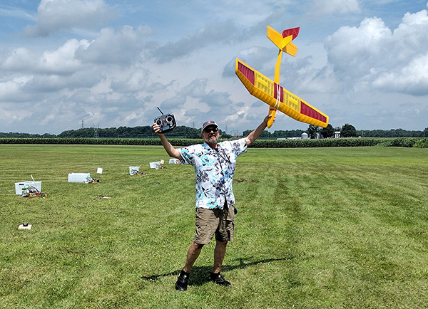 Man holding remote control plane on grassy field, smiling.