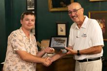 Two people shaking hands, one holding a 2023 award plaque, both smiling.