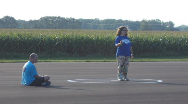 Man sitting and another standing on an asphalt road near a cornfield.