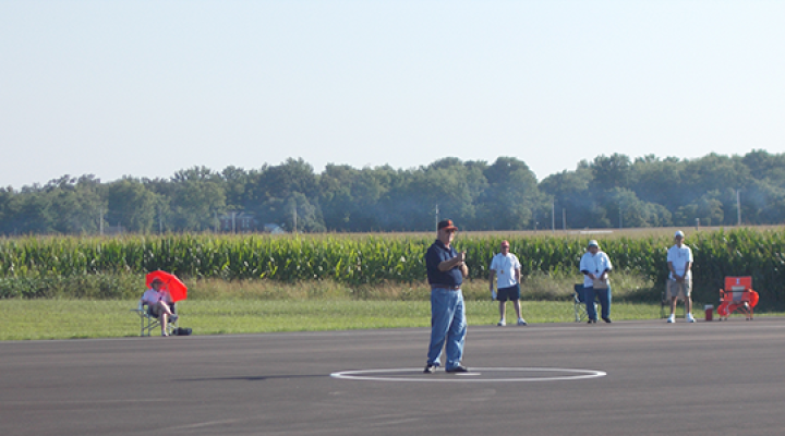 Man standing on tarmac with trees and fields in the background.