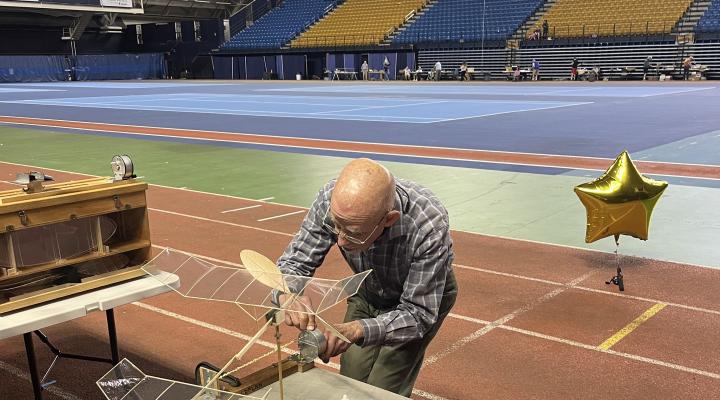Man adjusting a small, model propeller plane on an indoor track.