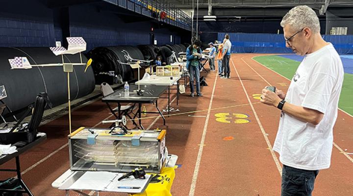 Indoor track event, man writes on paper near tables with equipment and flags.