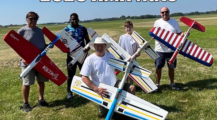 Five people holding model airplanes on a grassy field.