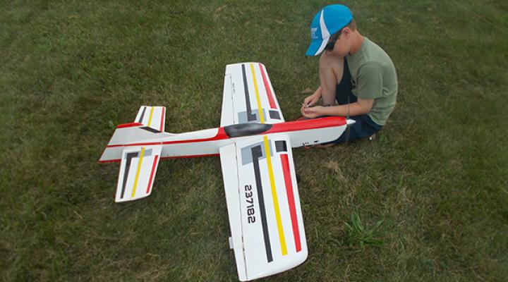 Boy assembling model plane on grass.