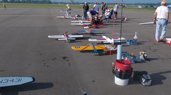 Toy airplanes lined up on a runway, people preparing them for flight.