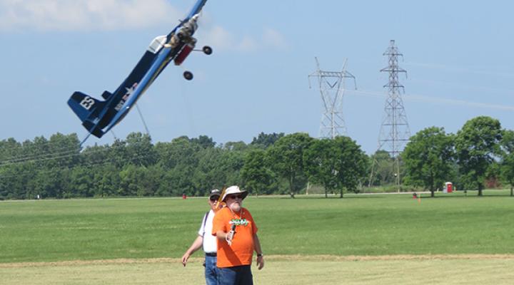 Remote-controlled plane flies low over a grassy field with power lines in the background.
