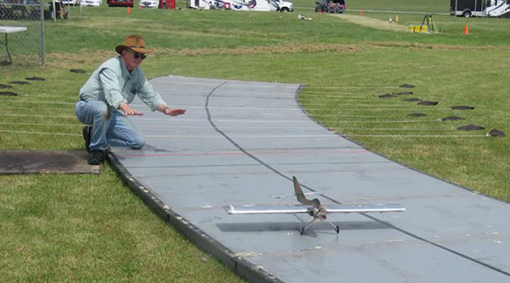 Man guiding small model airplane on a runway in a grassy field.