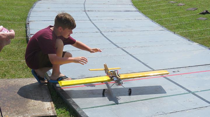 Boy kneeling, preparing a yellow model airplane on a raised track.