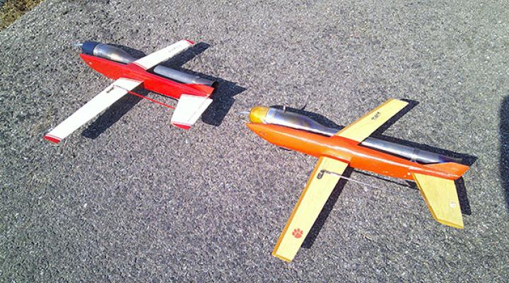 Two model airplanes on pavement, one red and white, the other orange and yellow.