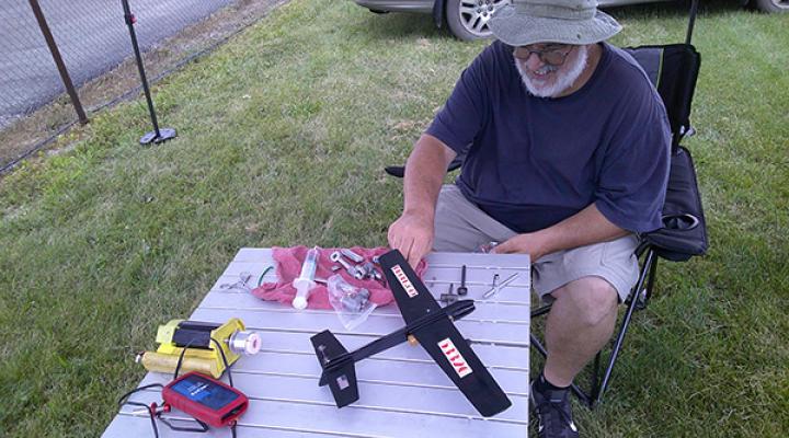 Man assembling model airplane outdoors on a table.