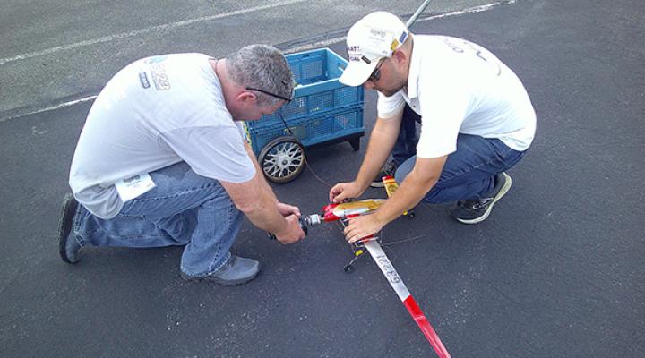 Two men kneeling, assembling a small model airplane on pavement.