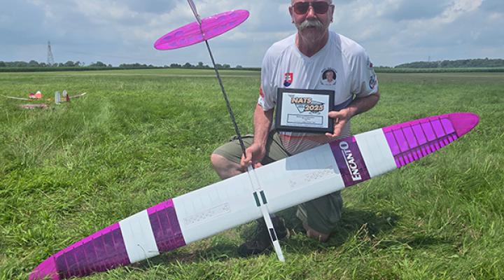 Man kneeling on grass with a model glider and holding a plaque.