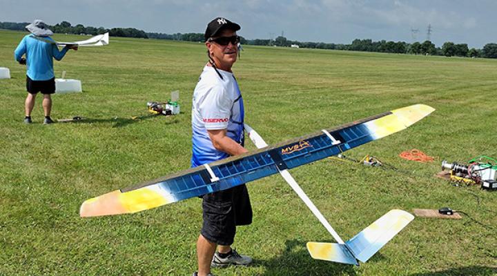 Man holding a large model airplane in a grassy field.