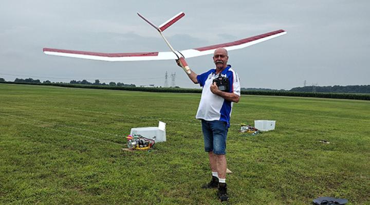 Man in a field holding a large model glider, remote control in hand.