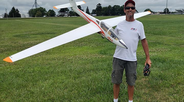 Man holding a large model airplane on a grassy field.