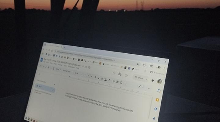 Laptop screen displaying a document, set against a dimly lit, post-sunset sky.