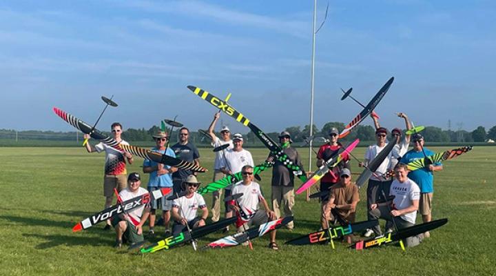 Group of people holding model aircraft on a grassy field.