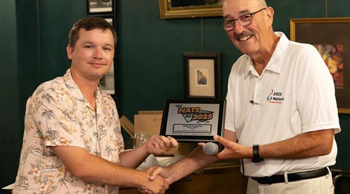 Two people shaking hands, one holding a 2023 award plaque, both smiling.