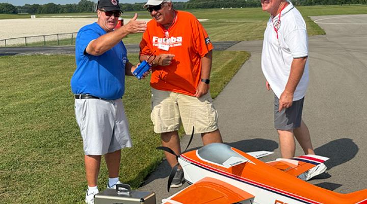 Three men laughing near a model airplane on a runway.