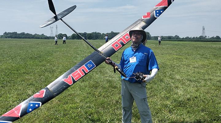 Man holding large model glider on grassy field.