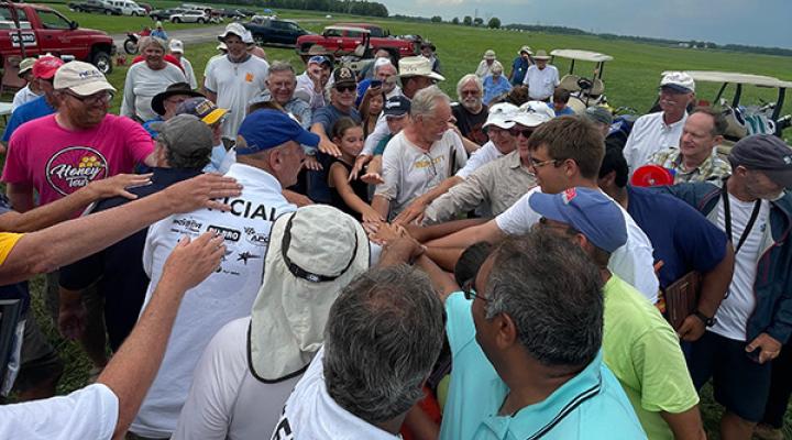 Group of people in a field, hands joined in the center.